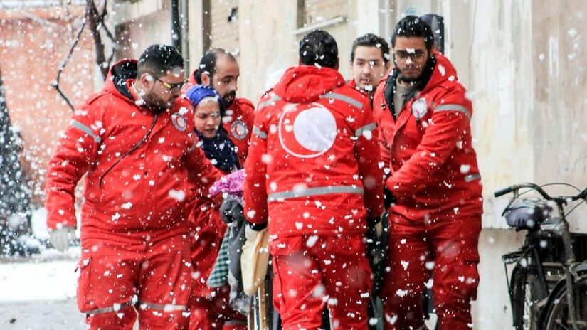 Une équipe d'ambulanciers du Croissant-Rouge syrien déplace un patient sur un brancard dans la neige à Homs, vers une ambulance en attente.