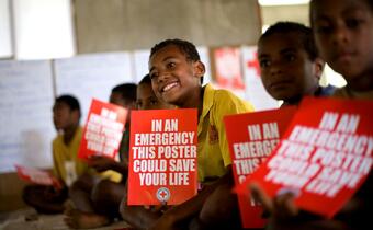 A group of young boys in Fiji hold up posters as they take part in a training session in their village on disaster preparedness, including how to prepare and respond to floods, cyclones, earthquakes and tsunamis