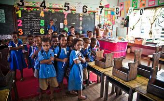 A group of young children in Fiji stand in their classroom which has been flooded many times in the past few years