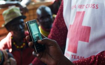 A Kenyan Red Cross volunteer helps a community in Turkana affected by drought and conflict to access emergency cash assistance via mobile phone