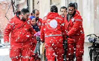 A team of medical workers from the Syrian Arab Red Crescent move a patient on a stretcher towards a waiting ambulance in the snow in Homs