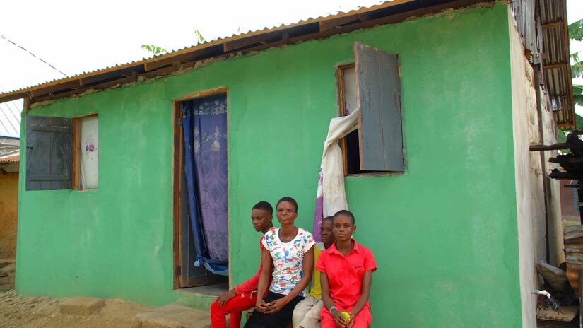 Gladys Ajiri (center) sits with three of her children in front of her new home, built using concrete blocks. Her earlier home, made from traditional mud construction, was washed away by the floods in 2023.