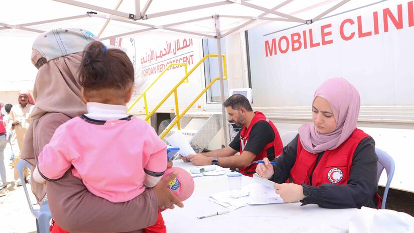 En el campamento de Al-Lubban, Jordania, una mujer y su bebé reciben asistencia médica de una clínica móvil de salud de la Media Luna Roja de Jordania.
