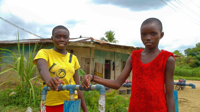 Two sisters, Juliet and Constance Elorghor, gather water from a new water source established by the Nigerian Red Cross in their community after floods in 2023.  14-year-old Juliet and 9-year-old Constance say the ready availability of water means they spend less time going to get water and more time in school.