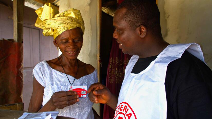 A volunteer with the Nigerian Red Cross provides a cash card to Miriam Abide, whose home was destroyed by the floods and then later rebuilt by the Nigerian 